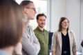 Foto einer Gruppe von drei jungen Kollegen, die sich in einem hellen Büro auf Augenhöhe unterhalten und lächeln.